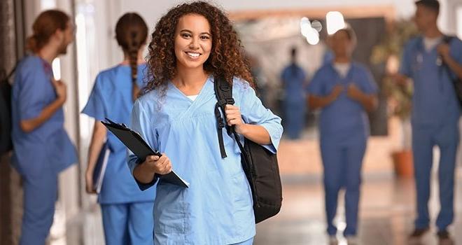 一个穿着护士服的女人拿着背包和活页夹.