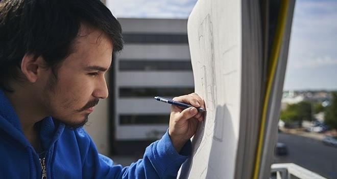 一个人在城市里用铅笔在画架上的大画布上画画.