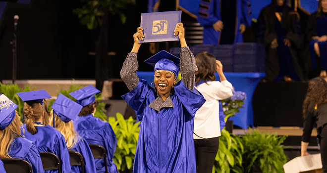 TCC Graduate in cap and gown hold diploma cover over her head.