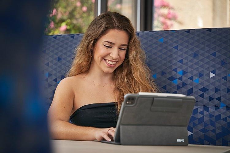 微笑的TCC学生坐在桌子前，在她的平板电脑上工作.